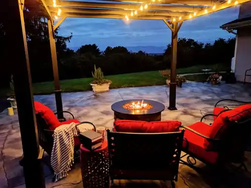 Paver patio with a pergola and fire table at dusk